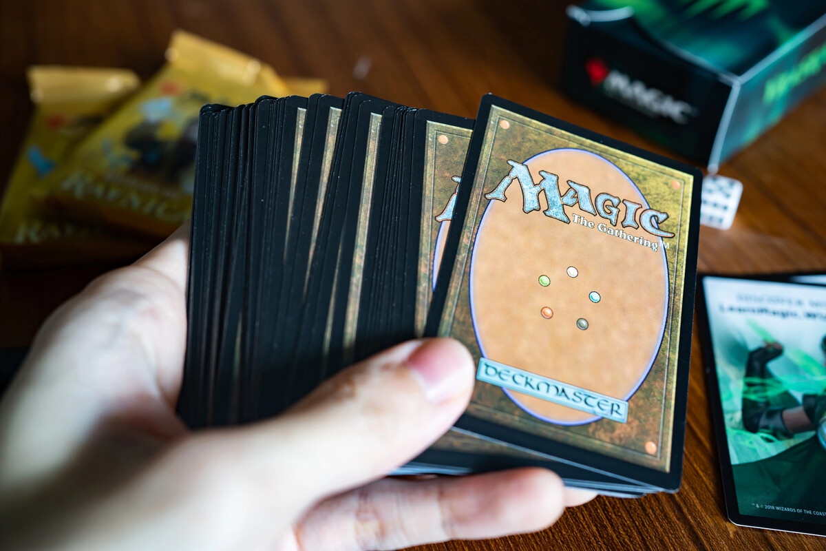 MTG hand holding a deck showing the Deckmaster card back on a table