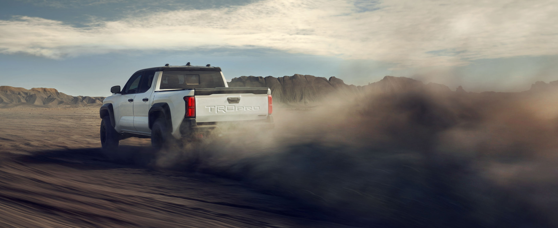 2025 Toyota Tacoma at Bobby Rahal Toyota in Mechanicsburg, PA | Rear view of a white 2025 Tacoma driving off on a dirt road