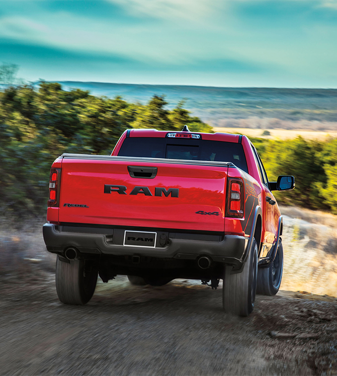2025 Ram 1500 at Delaney CDJR of DuBois | Rear profile of a red 2025 RAM 1500 Rebel edition driving down a hill