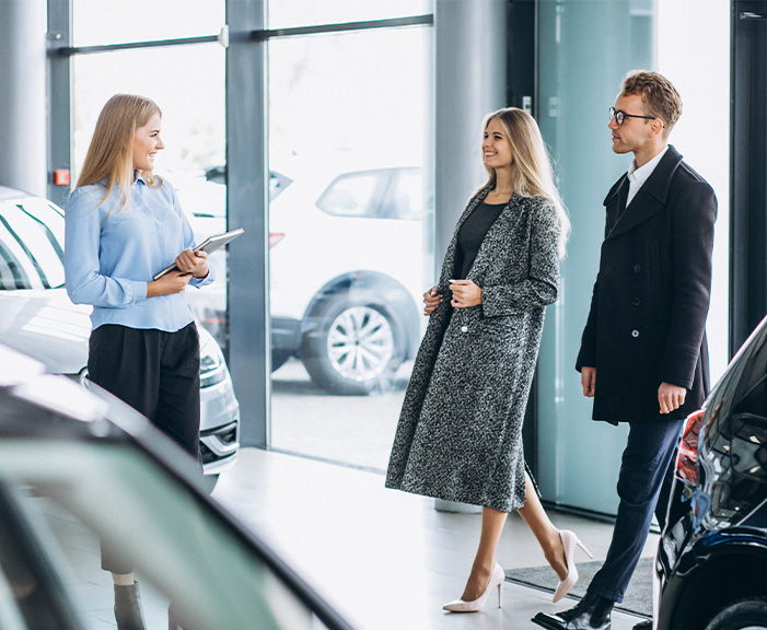Sell us your car | Couple walking into dealership about to talk to sales associate Sell us your car | Couple walking into dealership about to talk to sales associate