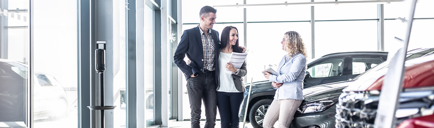 Sell us your car | Sell person leaning over car while talking to customers about selling their car Sell us your car | Sell person leaning over car while talking to customers about selling their car