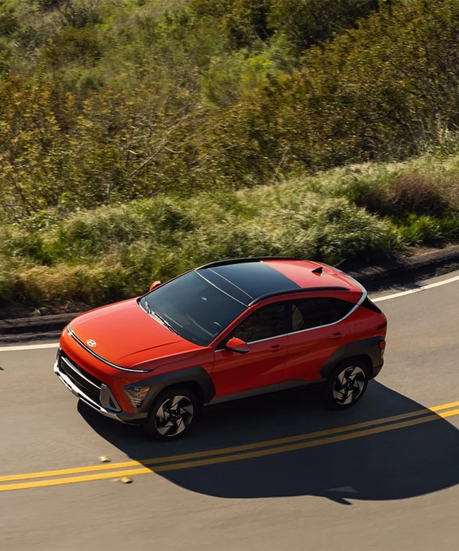  2025 Hyundai Kona at Delaney Hyundai of Dubois | Orange 2025 Hyundai Kona driving up a hill