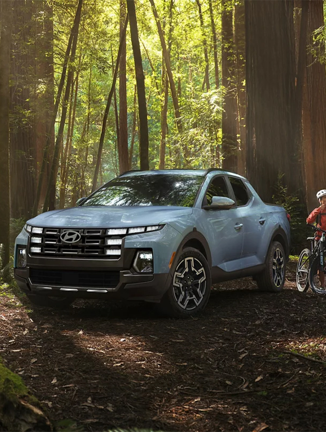 2025 Hyundai Santa Cruz at Delaney Hyundai of Dubois | light blue 2025 Hyundai Santa Cruz parked in the middle of the forrest while someone is about to go on a bike ride