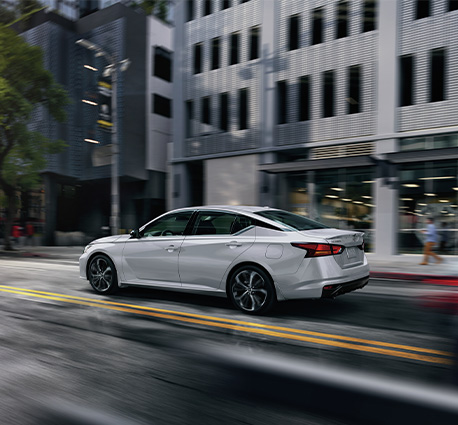 2025 Nissan Altima at Delaney Nissan of Greensburg | Rear profile of a white 2025 Nissan Altima driving down a city street at high speeds