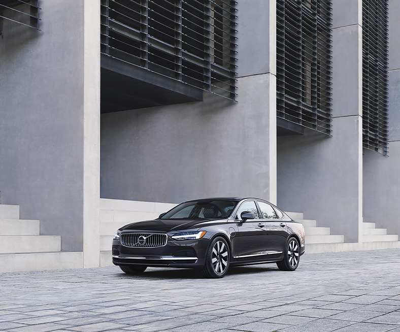 2025 Volvo S90 | Front profile of a black 2025 Volvo S90 Plug-in Hybrid parked in front of a grey building