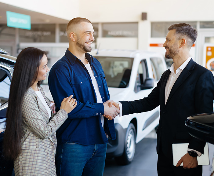 Sell us your car | couple shaking hands with sales representitive in black suit Sell us your car | couple shaking hands with sales representitive in black suit
