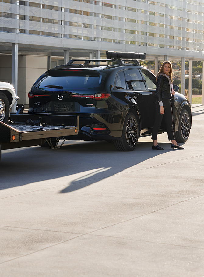2026 Mazda CX-70 & Mazda CX-70 PHEV at Lancaster Mazda | Woman stepping out of her parked 2026 Mazda CX-70 with a flat bed tow in the rear 2026 Mazda CX-70 & Mazda CX-70 PHEV at Lancaster Mazda | Woman stepping out of her parked 2026 Mazda CX-70 with a flat bed tow in the rear