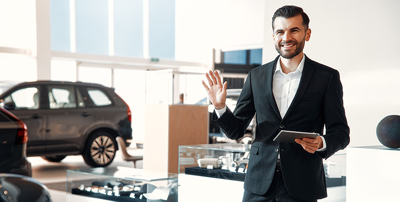 The Advantages of Buying a Car from a Dealership vs. a Private Seller. Learn more at Palmiero Toyota in Meadville, PA | Sales person in suit waving his hand at people walking into dealership
