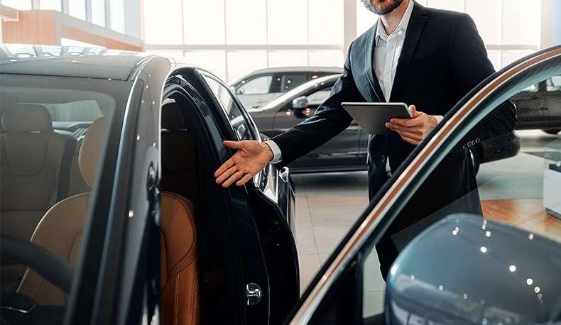 The Advantages of Buying a Car from a Dealership vs. a Private Seller. Learn more at Palmiero Toyota in Meadville, PA | Sales person in suit showing a new car model in the color black