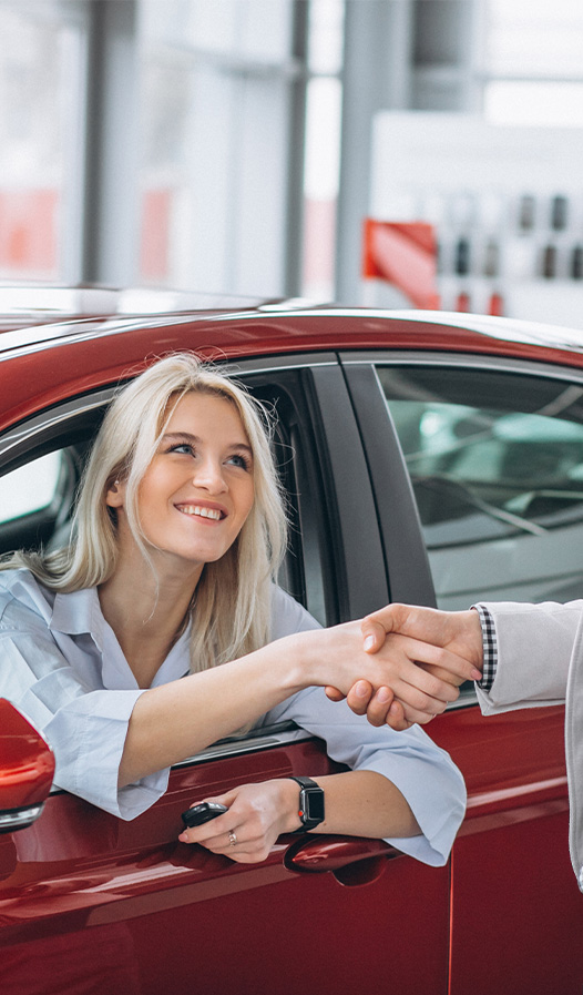 Buying New vs. Used. Learn more at Stetler DCJR in York, PA | Woman sitting in the drivers seat of a new car while shaking hands with someone outside of the car