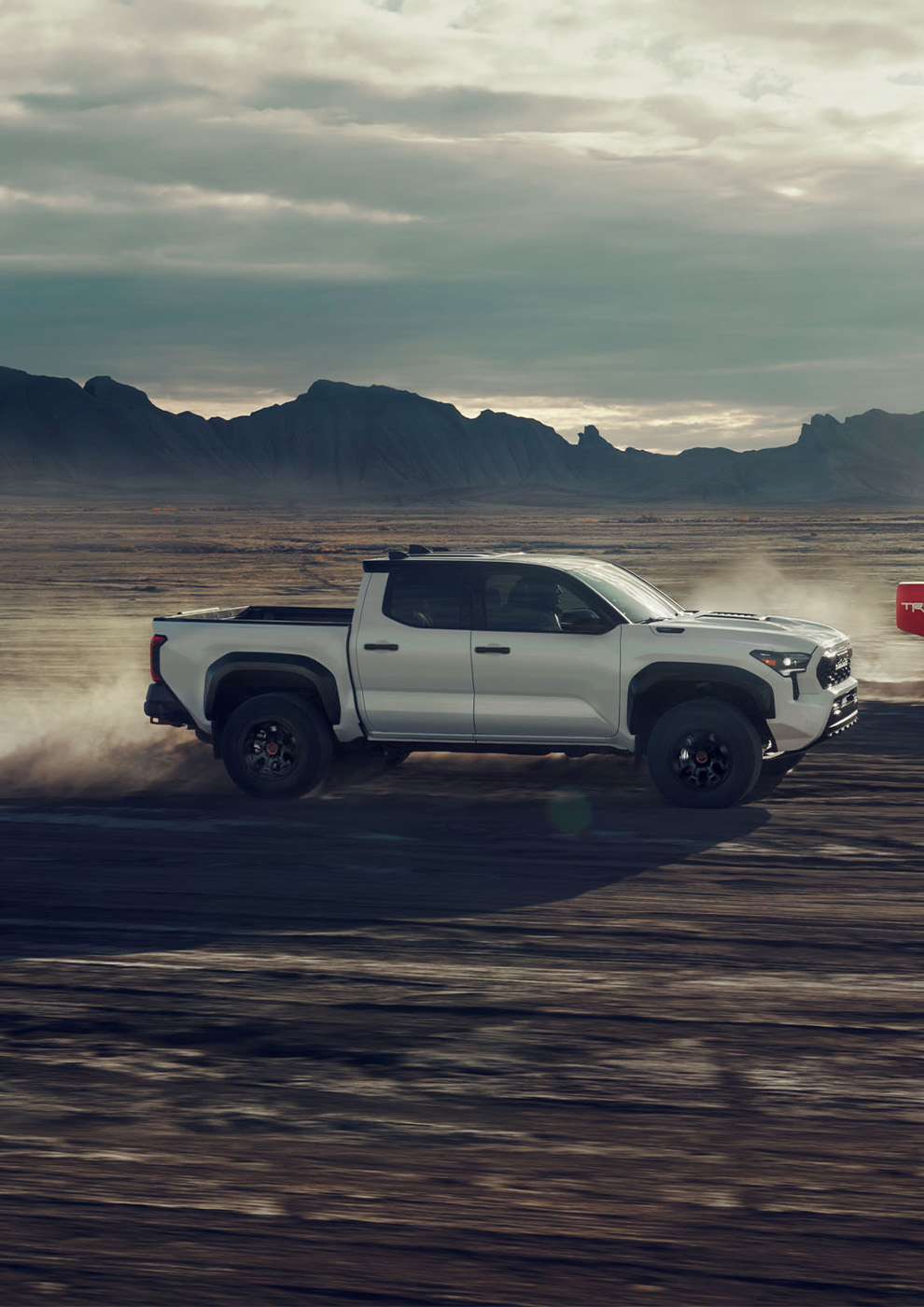 2026 Toyota Tacoma at CMA's Toyota of Martinsburg in Martinsburg, WV | Side profile of a silver 2026 Toyota Tacoma driving in the desert