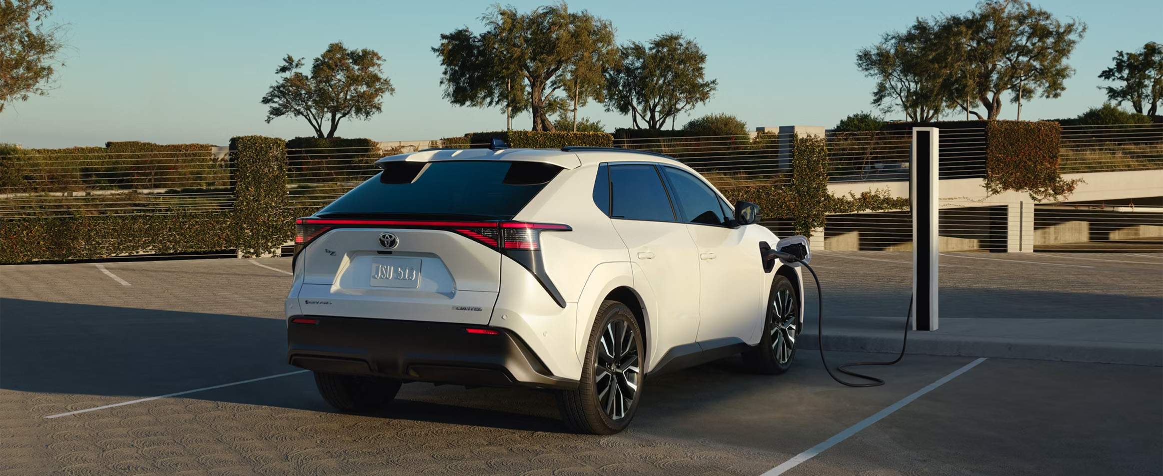 2026 Toyota bZ at CMA's Toyota of Martinsburg in Martinsburg, WV | Rear profile of a white 2026 Toyota bZ charging at a charging station