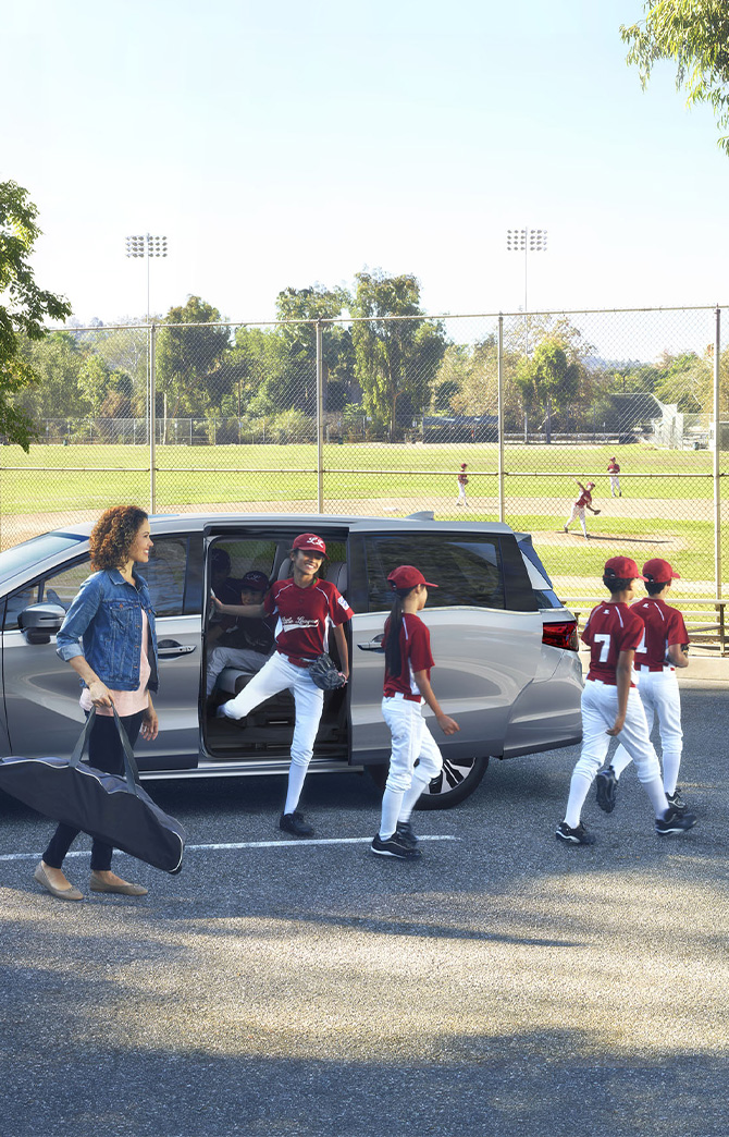 New 2026 Honda Odyssey at Delaney Honda | Kids baseball team walking out a parked 2026 Honda Odyssey in front of baseball field