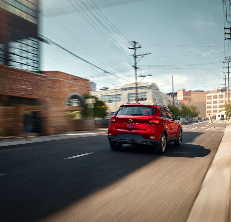  2026 Hyundai Venue at Delaney Hyundai of Dubois | Rear profile of a red 2026 Hyundai Venue driving fast down a city street