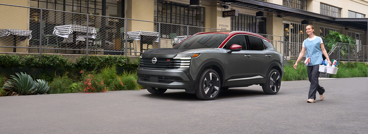 2026 Nissan Kicks at Delaney Nissan of Greensburg | Woman with cleaning supplies walking past a 2026 Nissan Kicks in the color grey 2026 Nissan Kicks at Delaney Nissan of Greensburg | Woman with cleaning supplies walking past a 2026 Nissan Kicks in the color grey