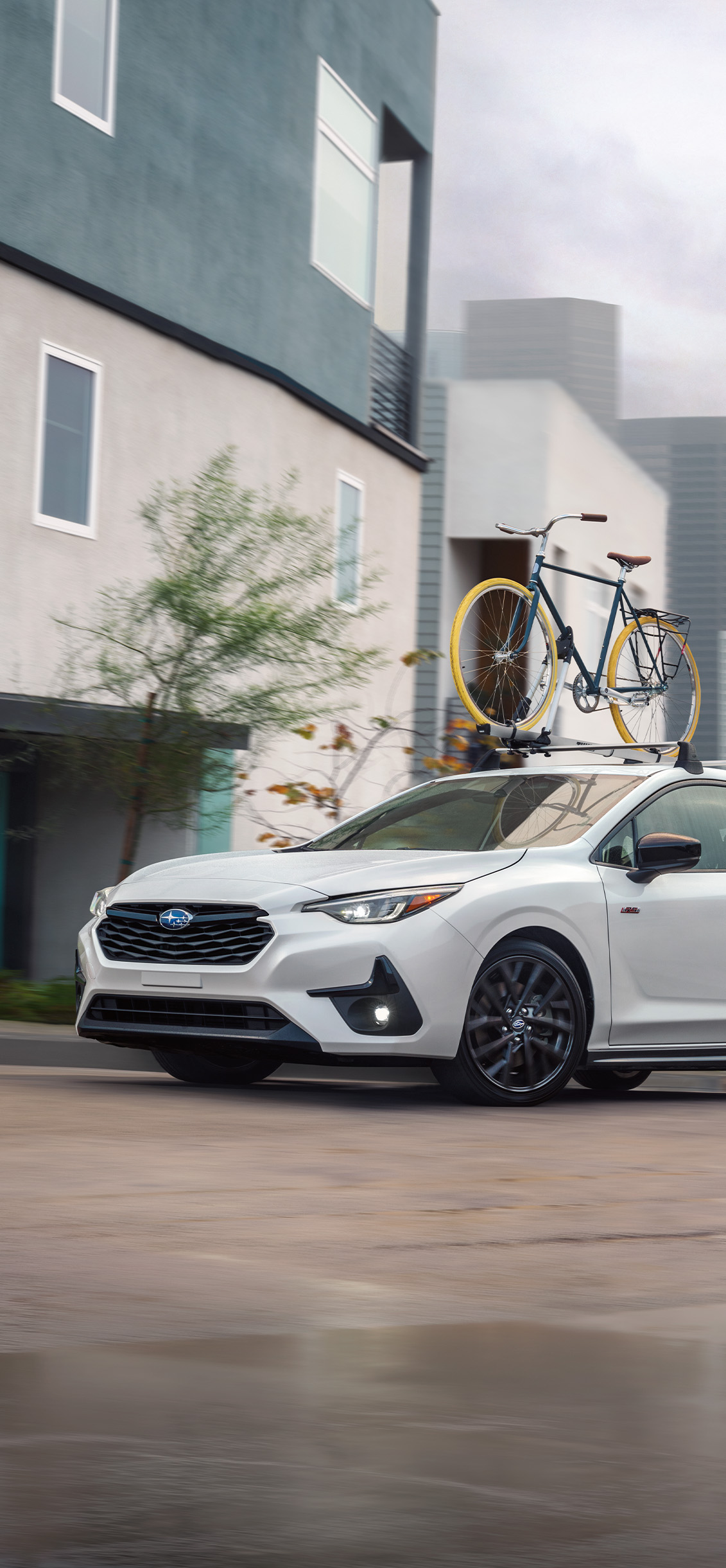 2026 Subaru Impreza at Delaney Subaru in Indiana, PA | White 2026 Subaru Impreza driving up the hill with a bike rack on the roof