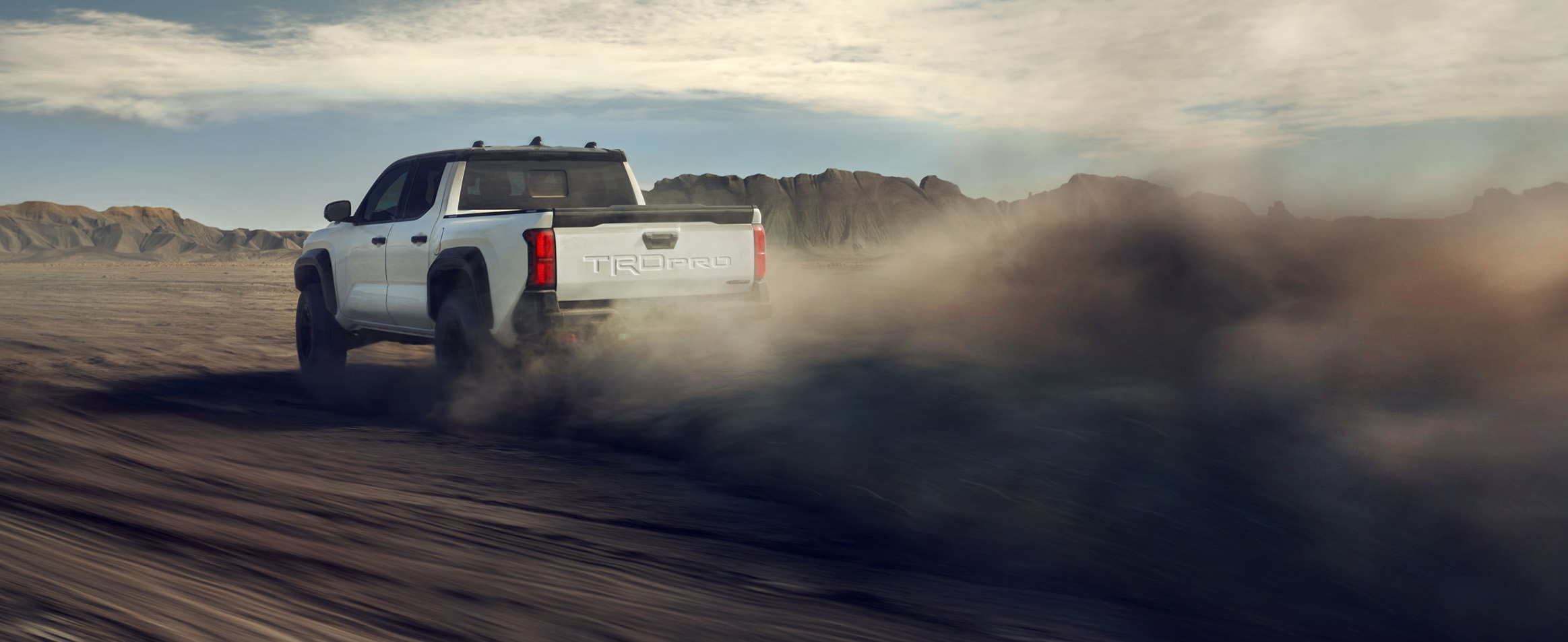 2026 Toyota Tacoma at Palmiero Toyota in Meadville, PA | Rear profile of a white 2026 Toyota Tacoma driving fast in the dirt