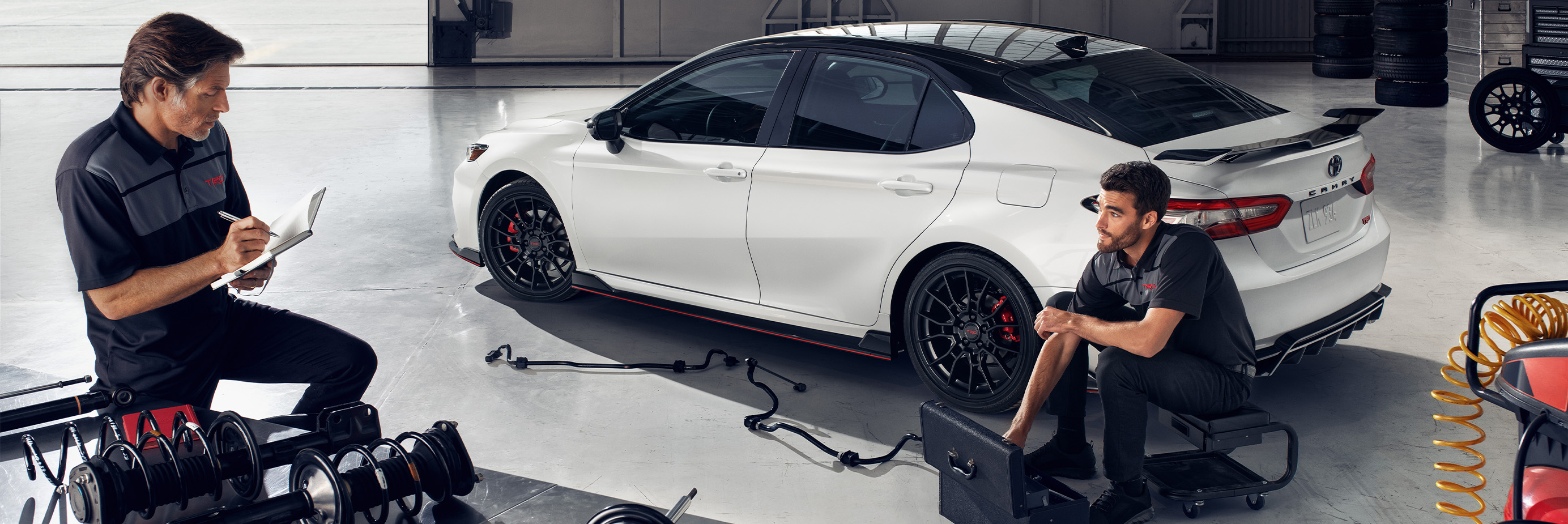 Register for Our New Owner's Clinic at Palmiero Toyota |  Two mechanics discussing about work while working in front of a white Toyota Camry