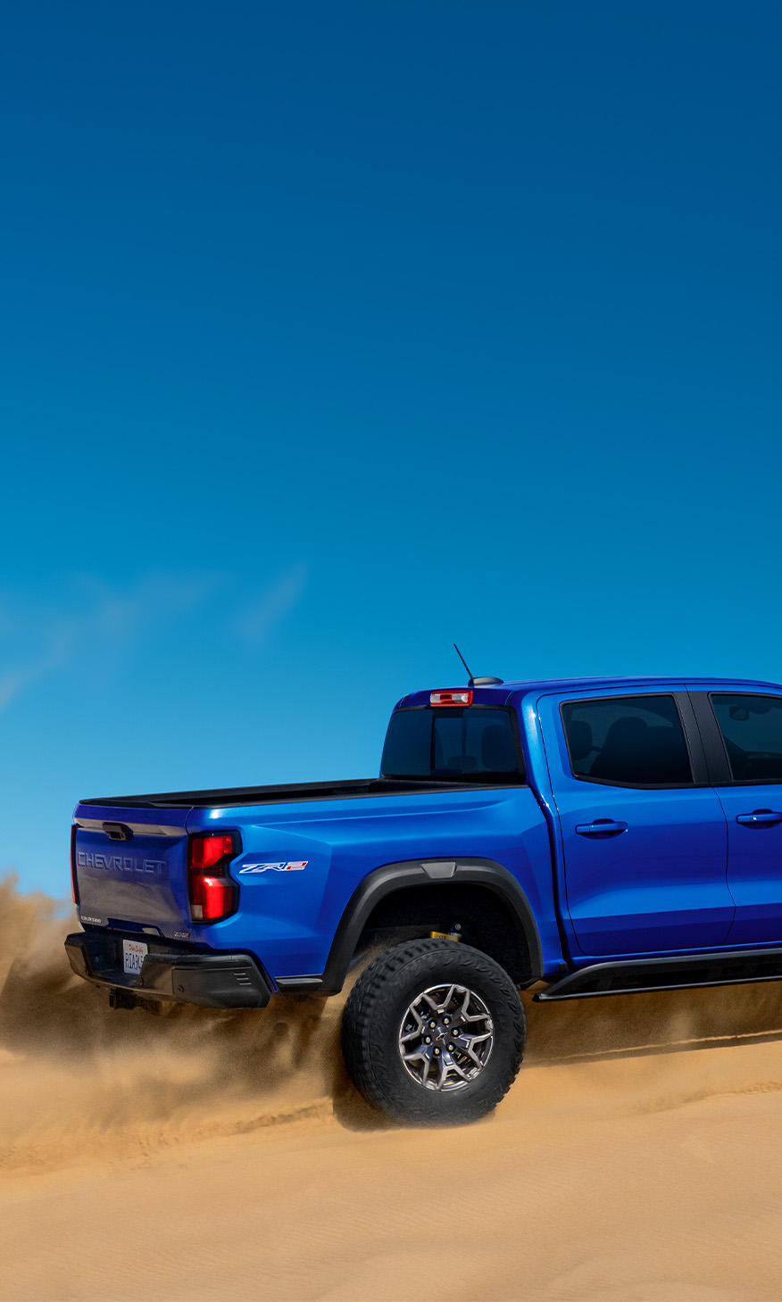 2026 Chevrolet Colorado at Sir Walter Chevrolet | Rear profile of a Blue 2026 Chevrolet Colorado driving in the desert 2026 Chevrolet Colorado at Sir Walter Chevrolet | Rear profile of a Blue 2026 Chevrolet Colorado driving in the desert