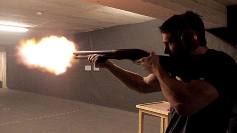 A man pulls the trigger of a gun, sending a colorful flare soaring into the air.