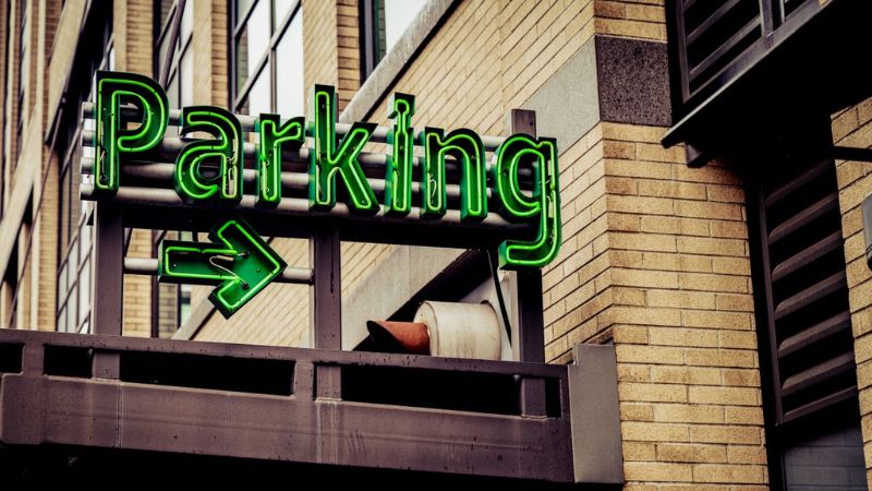 Bright green neon sign reading “Parking” with an arrow pointing right, mounted on a brick building.