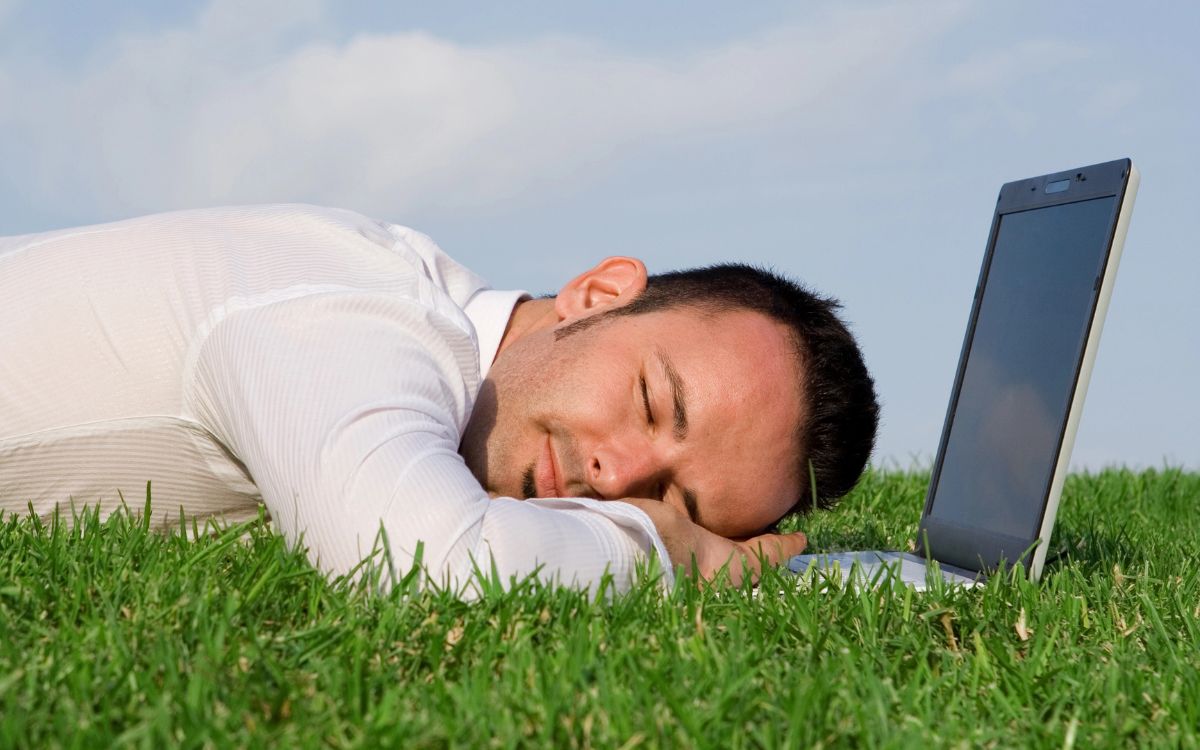 Ein Mann macht einen Power-Nap am Schreibtisch vor seinem Laptop