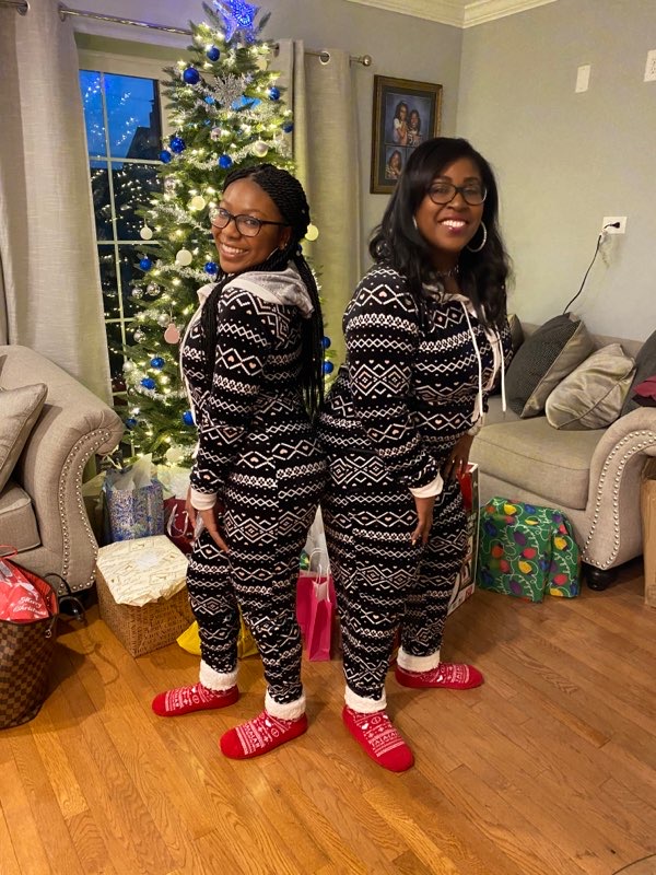 Mother and daughter standing back to back in pajamas smiling. 