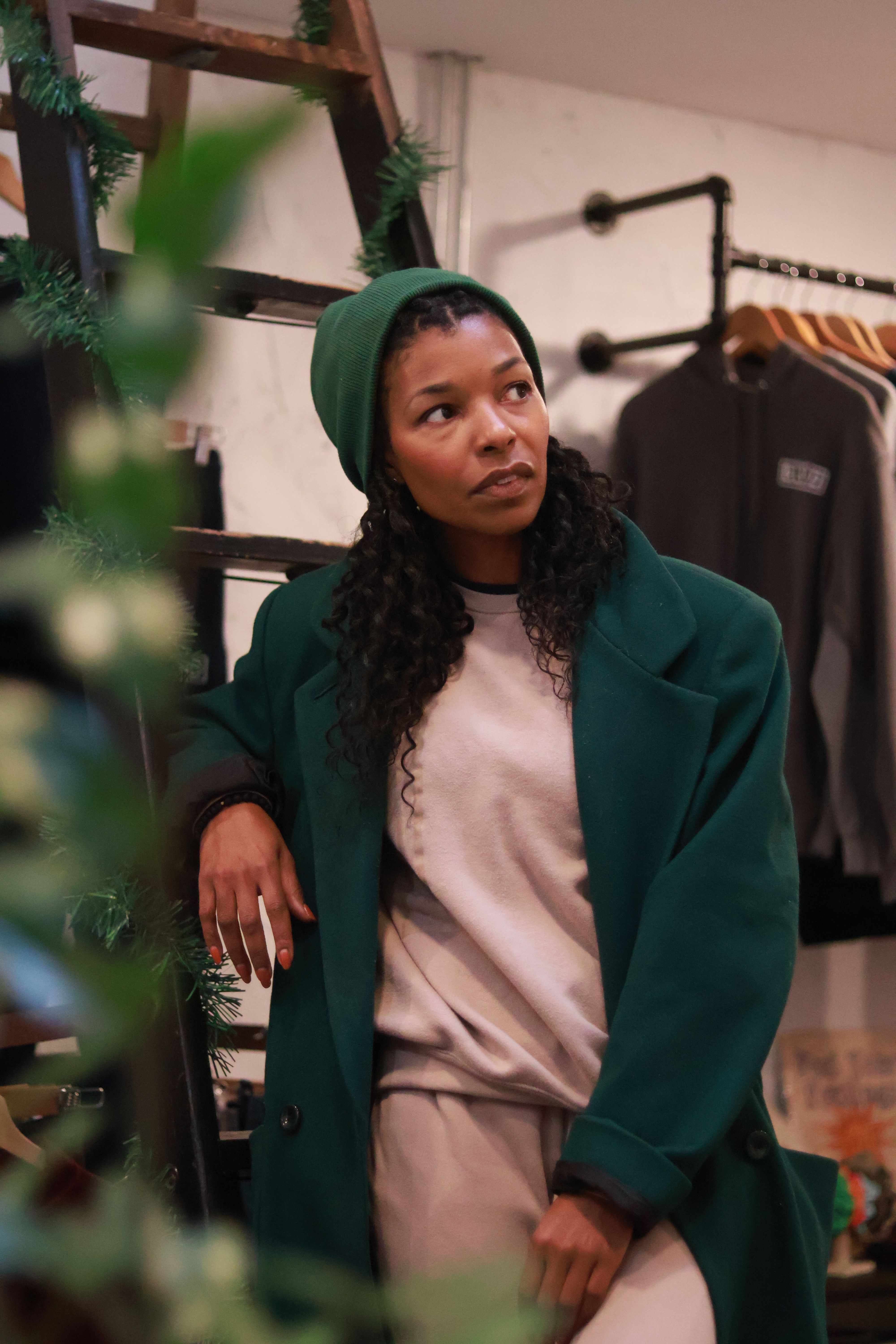 Photo of a light skin black woman wearing a dark green beanine and a dark green overcoat on top of a beige sweatsuit 