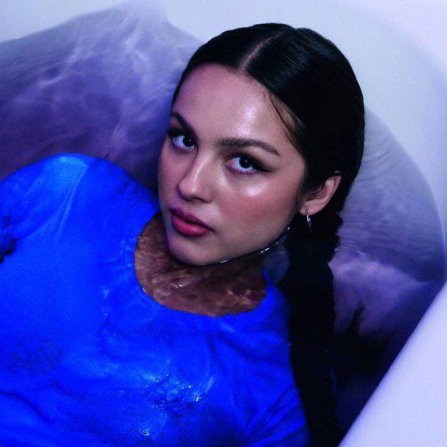 Olivia Rodrigo lays in a bathtub filled with purple water. 