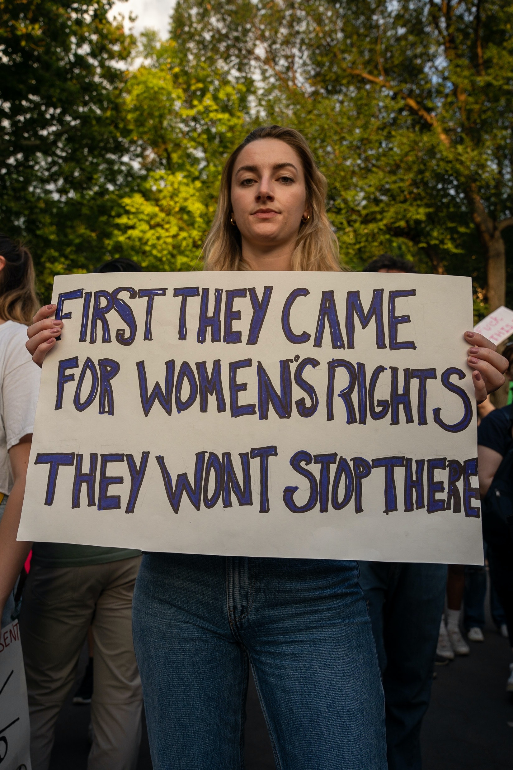 A young women holding a sign that reads "first they came for women's rights they won't stop there"