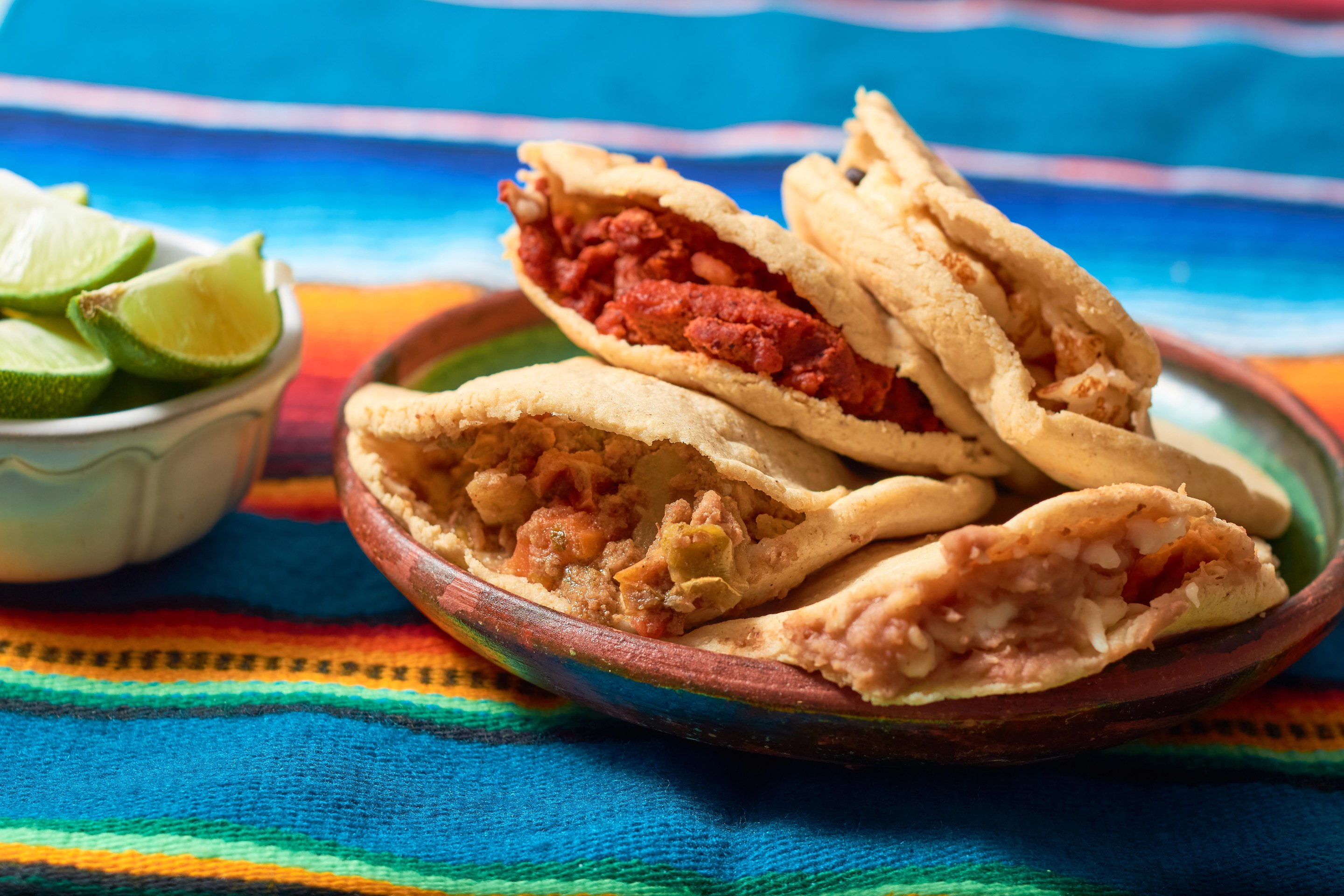 Two hand-made gorditas split open on a clay plate, one filled with chorizo and one with beans, next to lime wedges