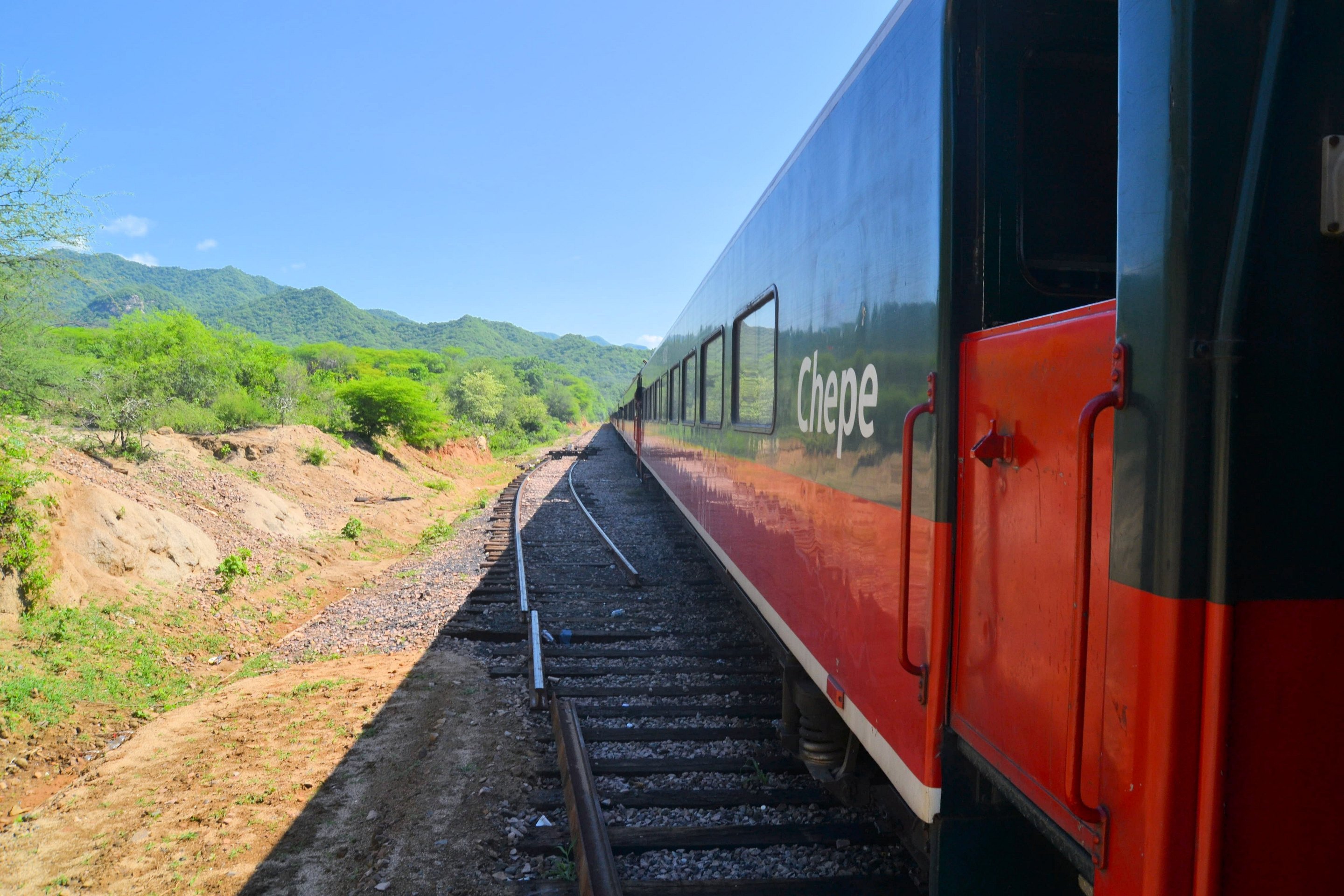 The red and cream cars of El Chepe on a straight stretch of track through dry brush country