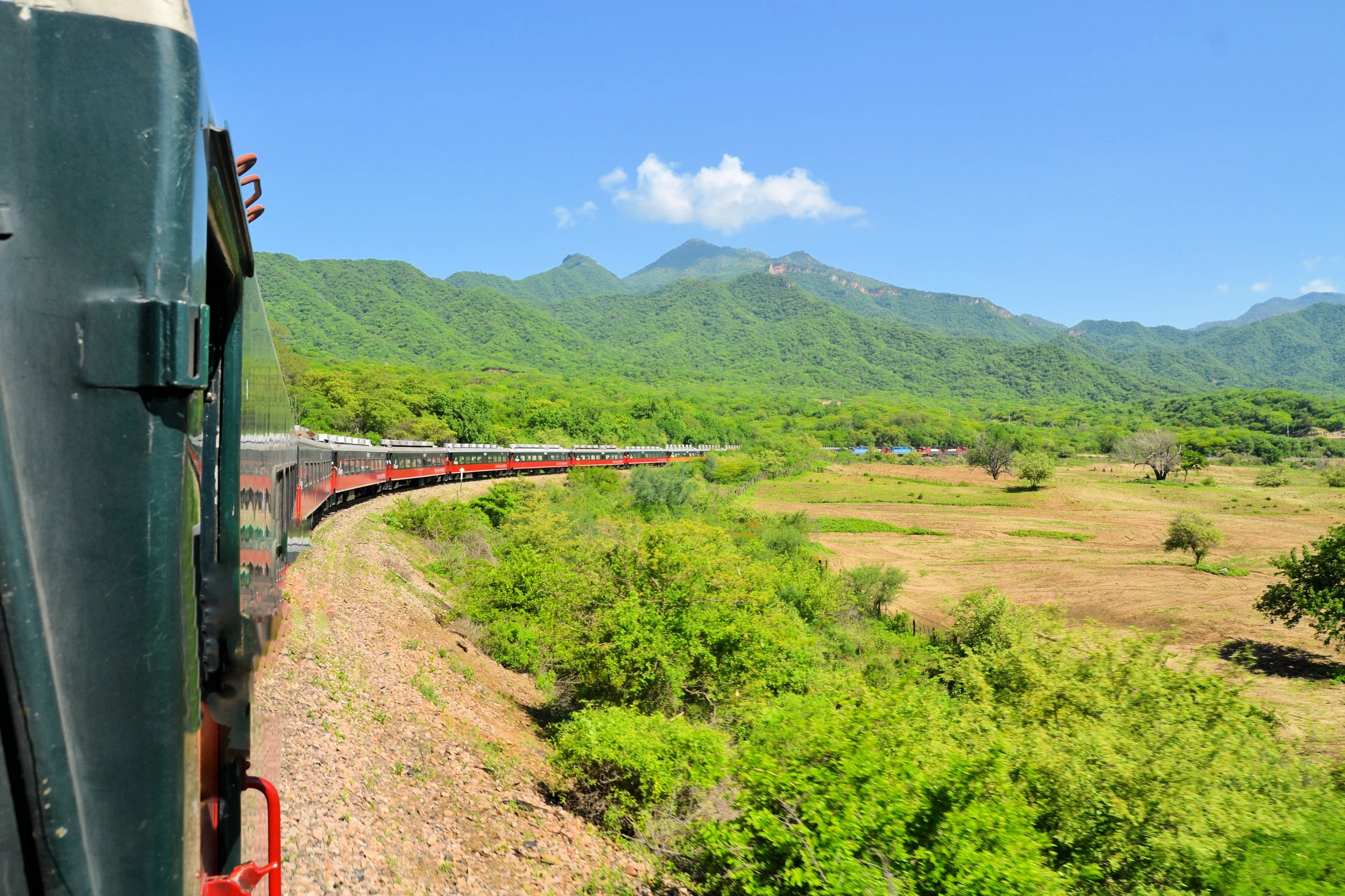 El Chepe curving through a wide green valley, the whole train visible from the last car