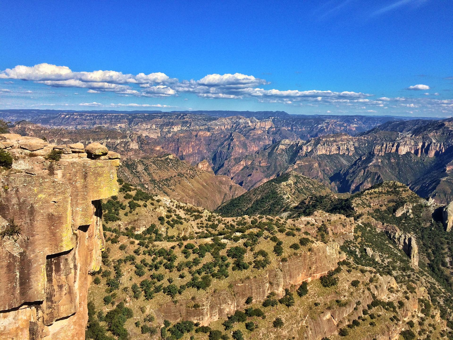 A rock ledge standing over the canyon, with green slopes and distant ridges beyond, at Divisadero