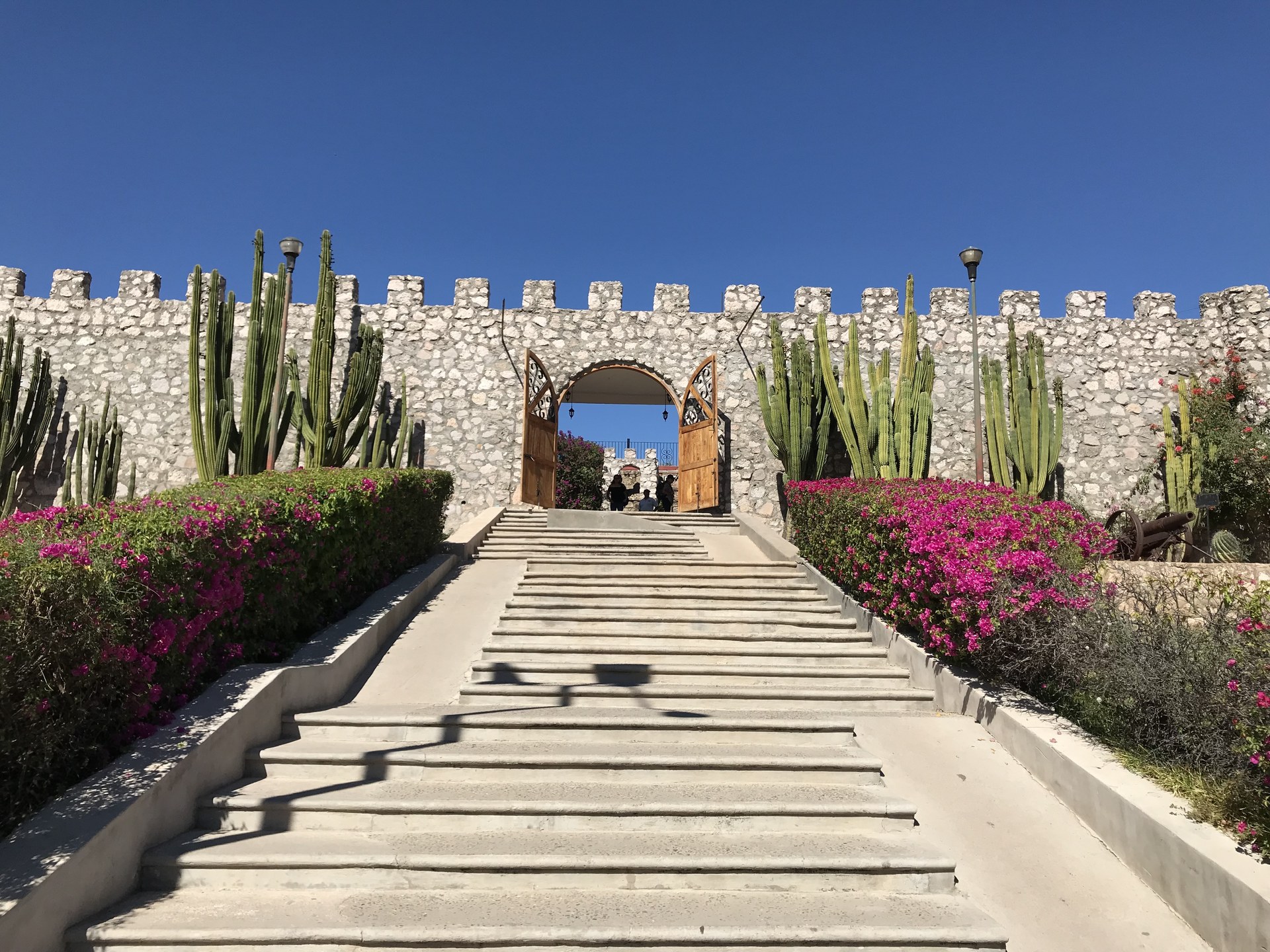 Stone steps lined with cacti and bougainvillea lead up to the gate of the fort-style museum in El Fuerte