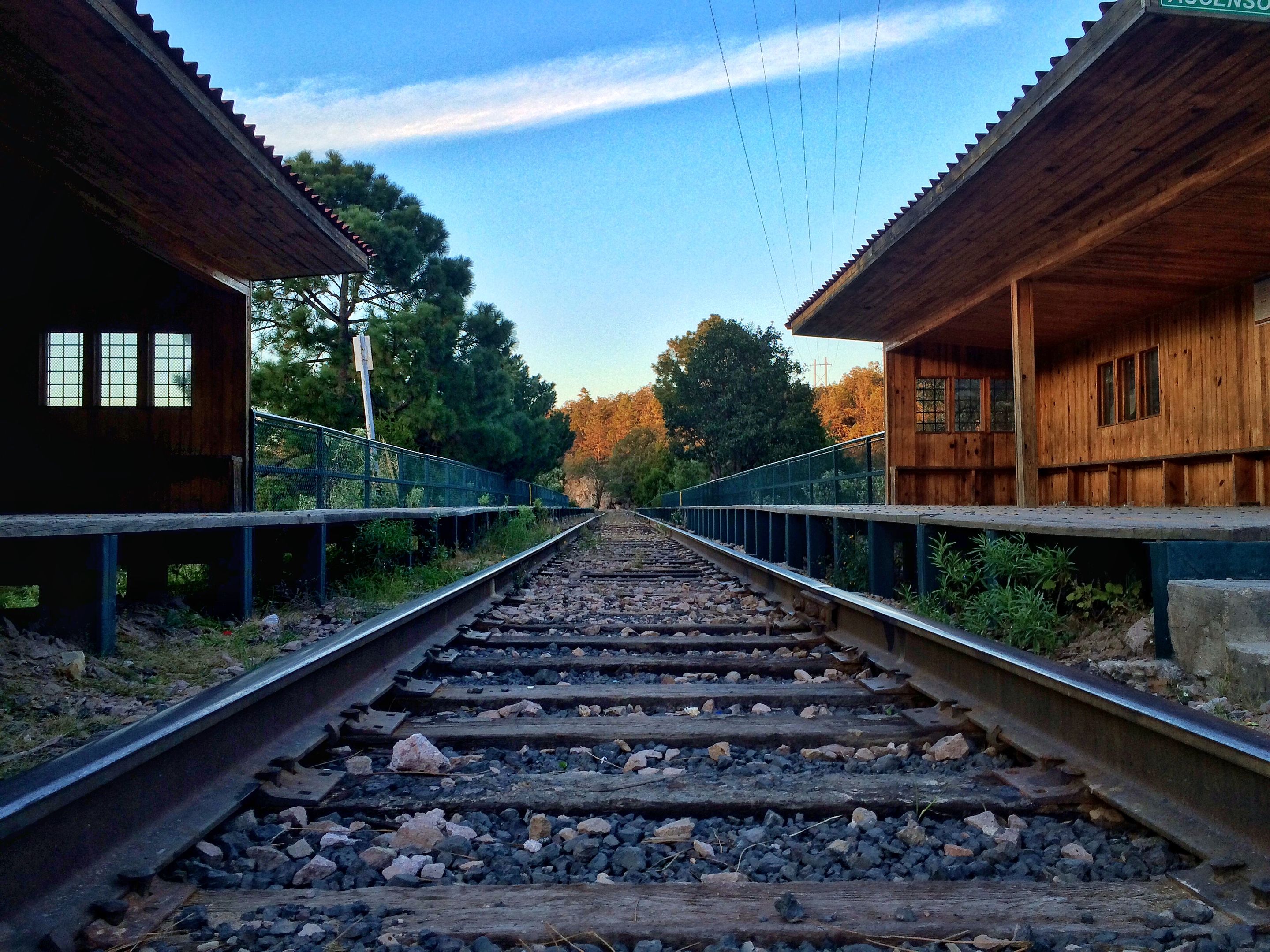 Track-level view of the rails running between the two wooden buildings of Posada Barrancas station