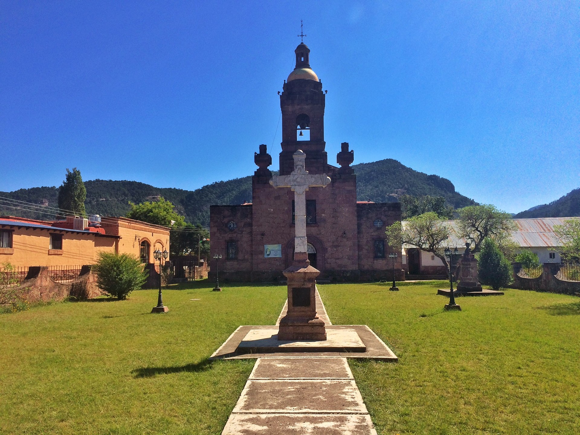 Die steinerne Missionskirche von Cerocahui hinter einer Rasenfläche und einem hohen Kreuz