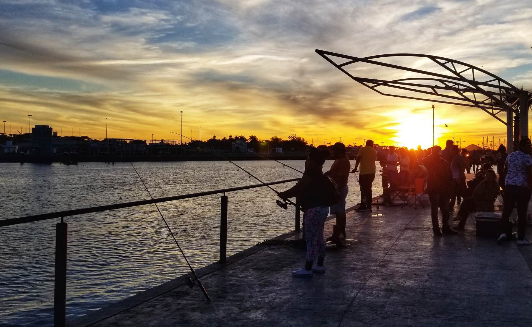Menschen angeln bei Sonnenuntergang von der Promenade in Topolobampo, die Sonne tief über der Bucht