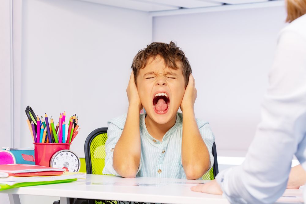 Screaming autistic boy close ears during lesson