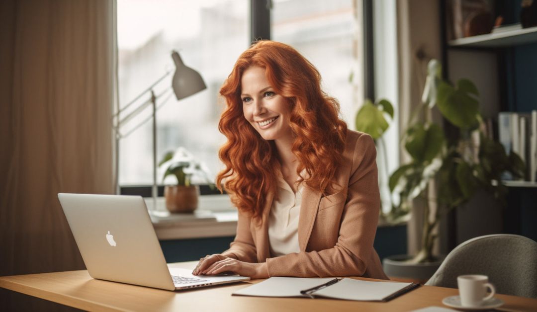 A Woman With Red Hair Sitting At A Desk With A Laptop.