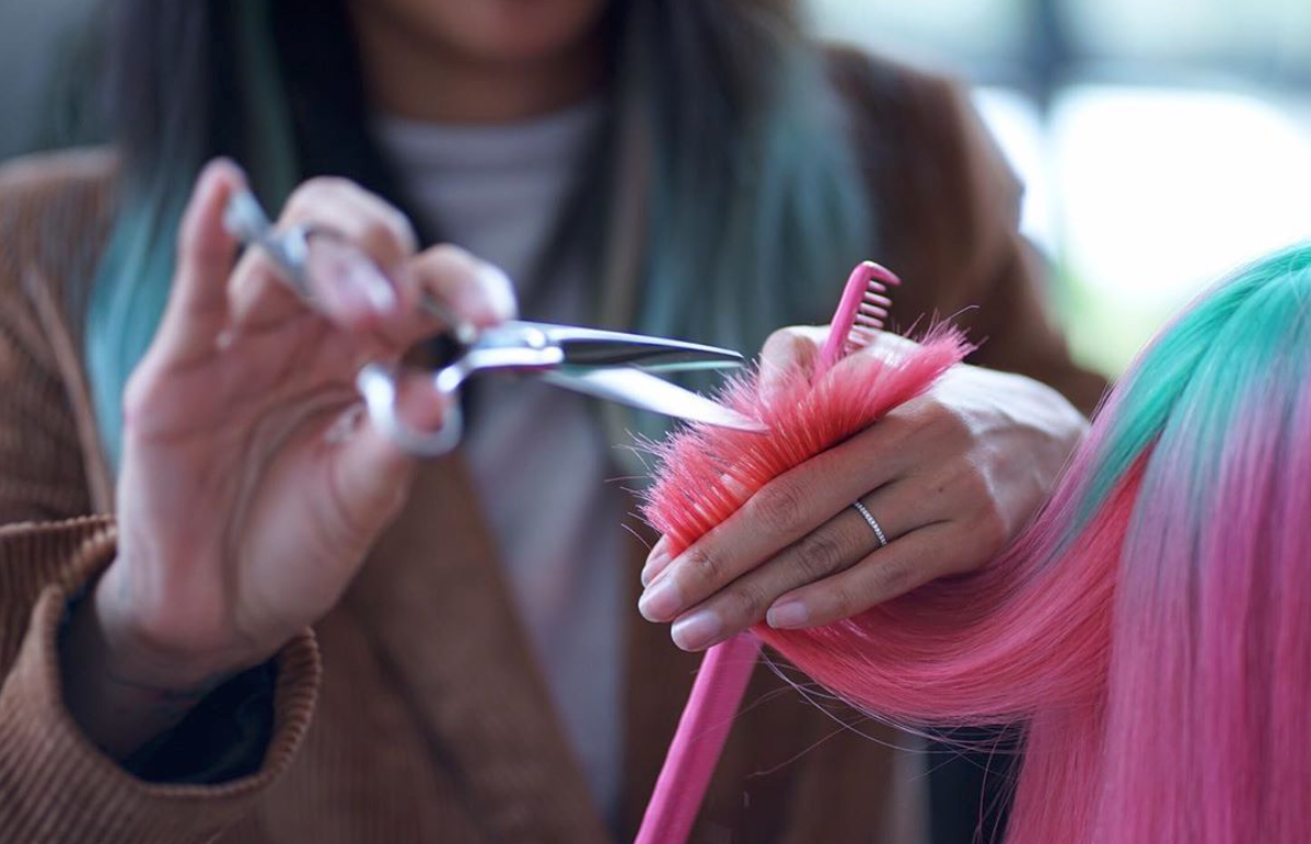 Styling and finals touches A picture depicting a hairdresser doing styling and final touches on pink hair
