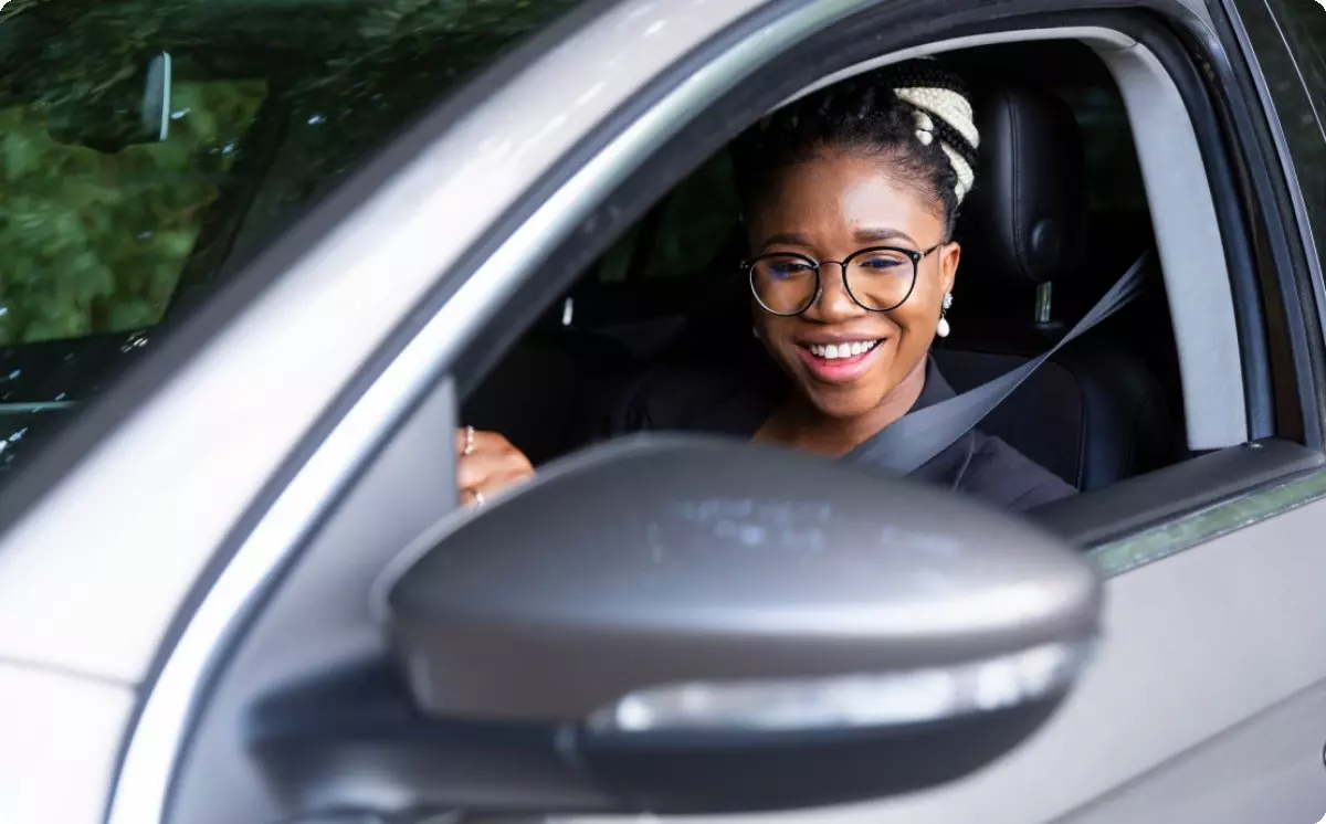 A woman driving and smiling at her side mirror