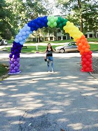 Sasha Dougherty standing under rainbow-colored balloon archway. (Anesia Meredith/Staff Writer)