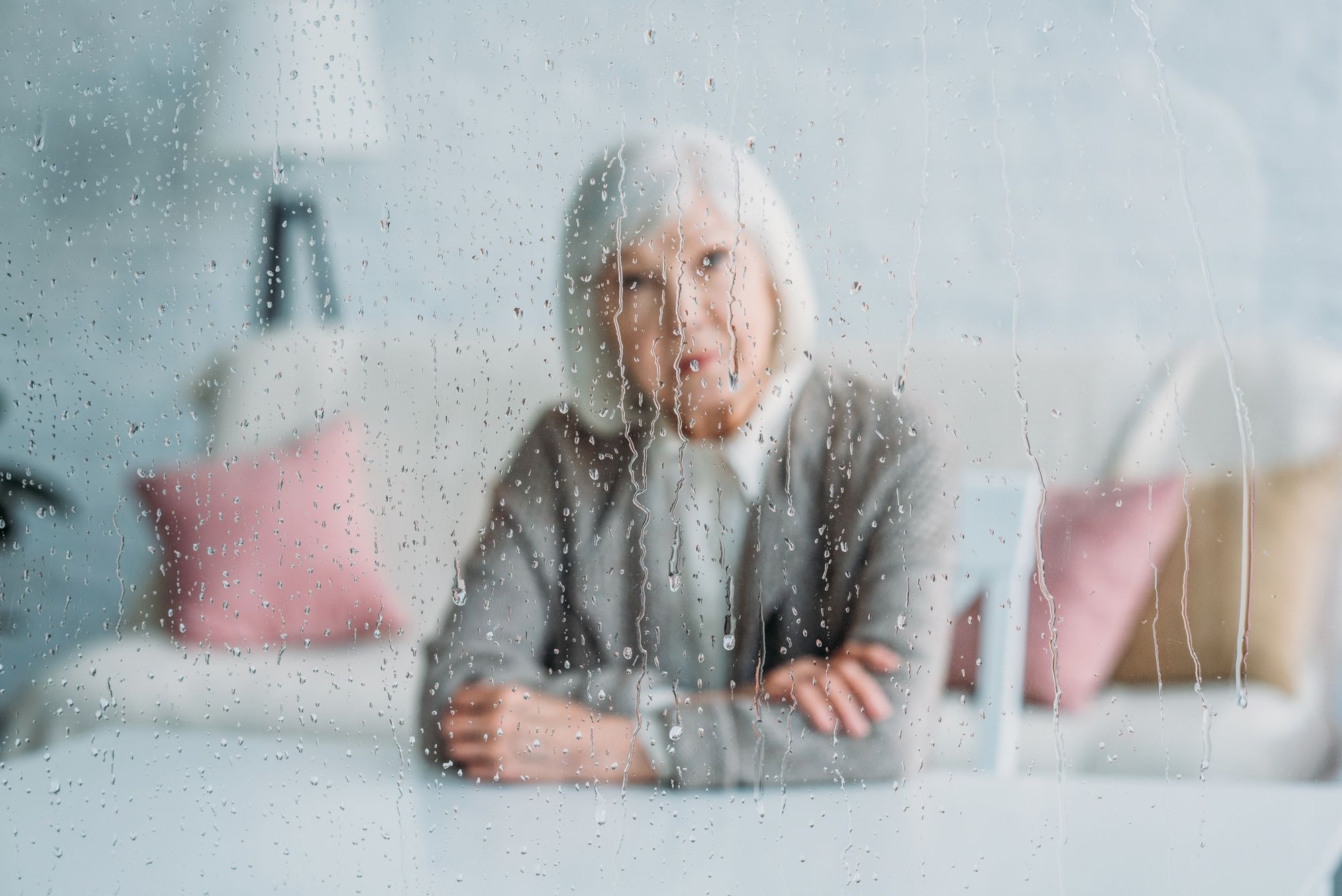 senior woman in knitted jacket sitting at table alone at home