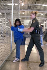 CBP Border Patrol agent conducts a pat down of a female Mexican being placed in a holding facility.