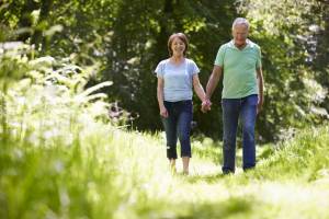 An elderly man and woman are walking through the country side holding hands