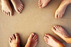 The feet of 3 people on a beach