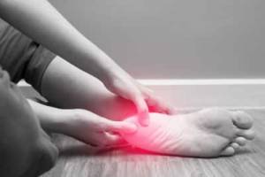 A woman holds her sore heel which is shown in red