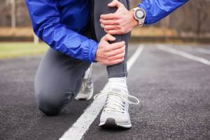 A man crouches down by the side of the road holding his left shin with both hands