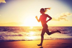 A confident looking woman is running on the Beach with the sun setting over the water